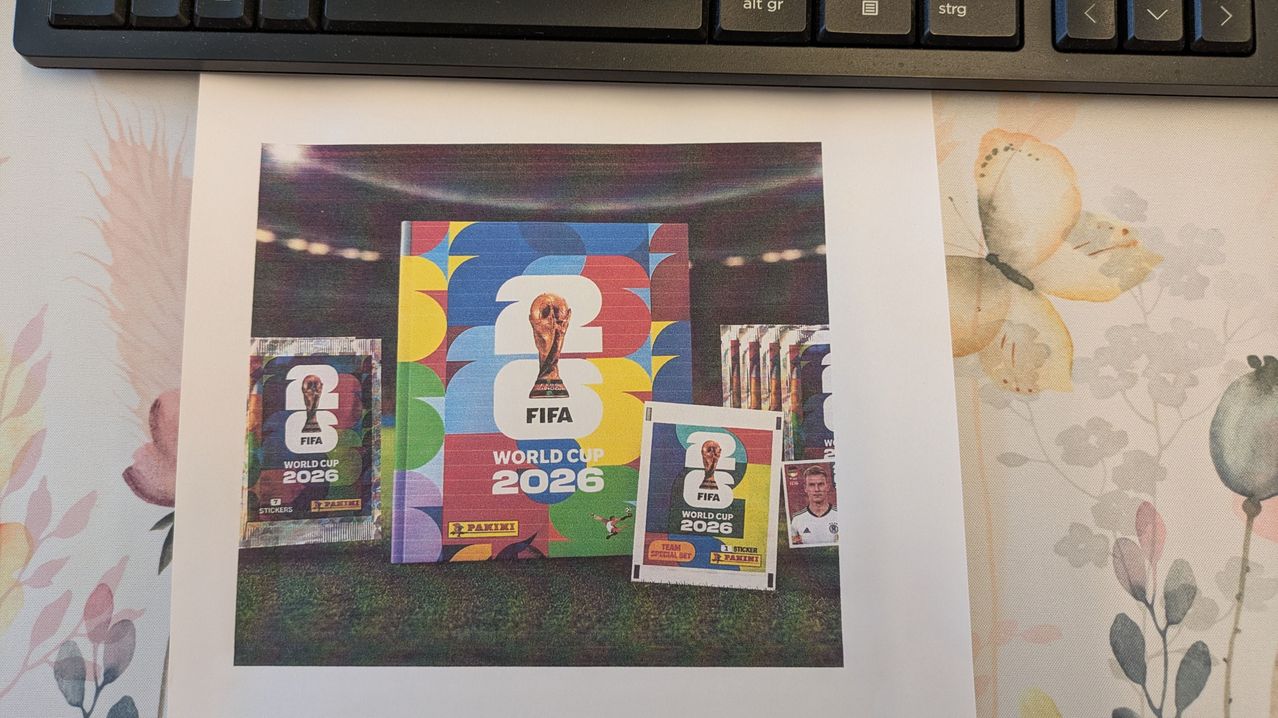 A collection of colorful FIFA World Cup 2026 stickers and cards on a white background with a blurry stadium in the background.