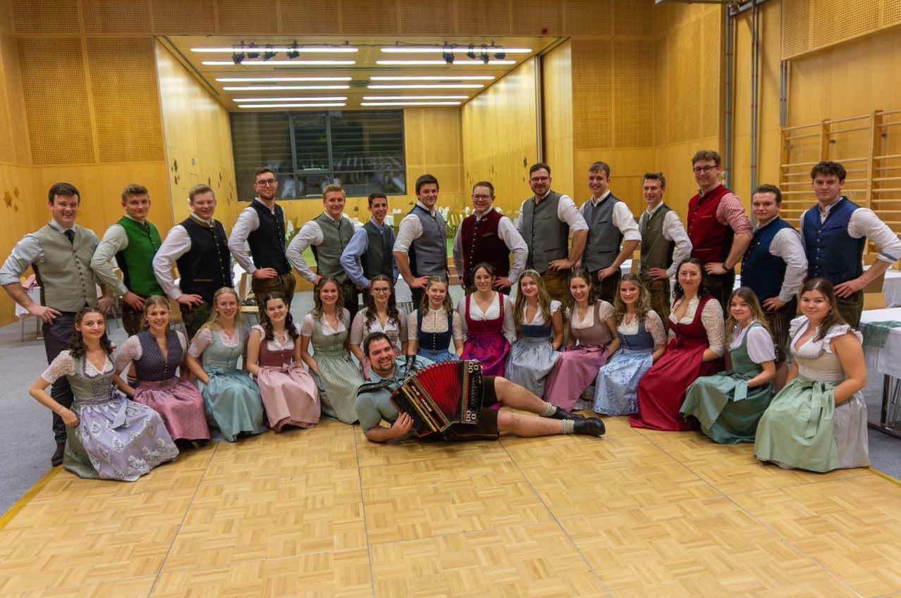 Eine Gruppe von Menschen in traditioneller Kleidung posiert für ein Foto in einem Raum mit Holzwänden.