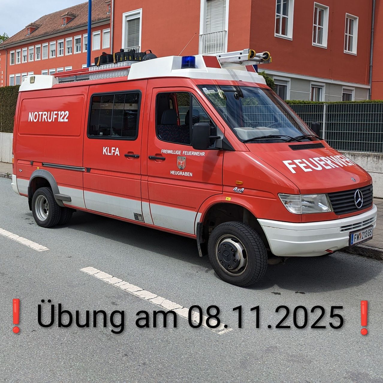 Ein roter Feuerwehr-Van mit der Aufschrift NOTRUF122 und FREWILLIGE FEUERWEHR an der Seite ist auf der Straße geparkt. Der Van steht in der Nähe eines roten Gebäudes mit mehreren Fenstern. Das Nummernschild zeigt FW21985. Das Bild hat einen Überlagerungstext, der lautet ! bung am 08.11.2025 !