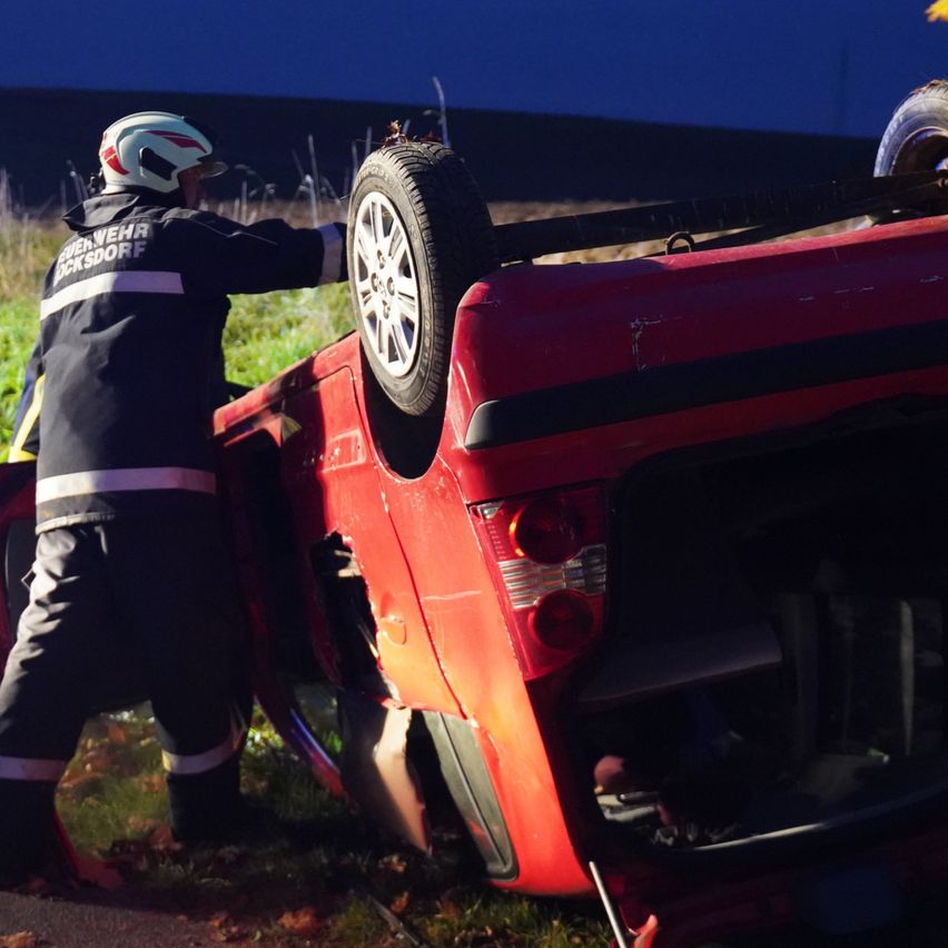 Ein Feuerwehrmann in Uniform zieht ein rotes Auto mit einem Rad vom Boden ab. Das Auto ist seitlich geneigt, wobei das Heck auf dem Boden aufliegt.