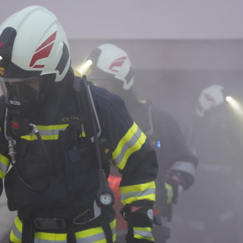 Ein Feuerwehrmann in voller Ausrüstung, einschließlich Helm und Maske, geht durch eine rauchige Umgebung. Ein weiterer Feuerwehrmann folgt ihm.