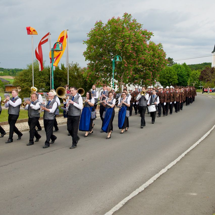 Ein Marschorchester tritt auf der Straße auf, wobei Musiker Trompeten, Posaunen und Trommeln spielen. Die Orchestermitglieder tragen einheitliche Uniformen und marschieren in Formation.