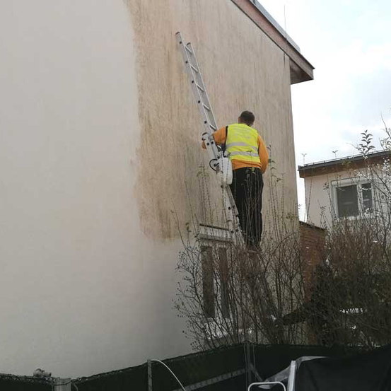 Ein Mann in einer gelben Weste steht auf einer Leiter und malt die Seite eines Gebäudes.