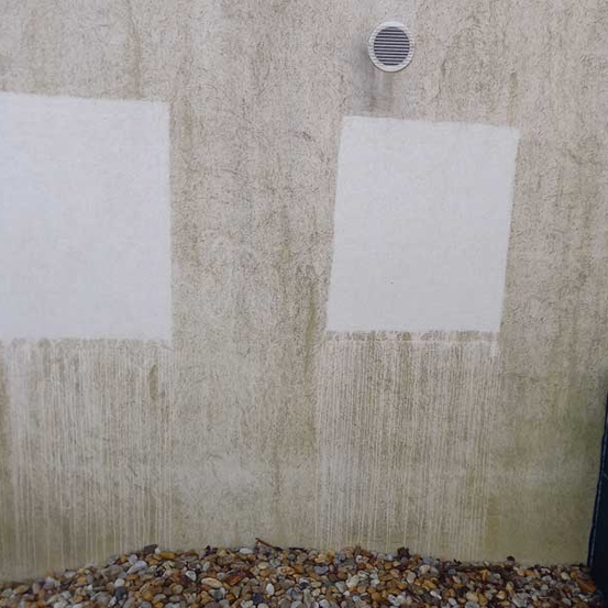 Eine Wand mit zwei weißen Flächen und Schmutzflecken. Unter den Flächen ist Kies verstreut.