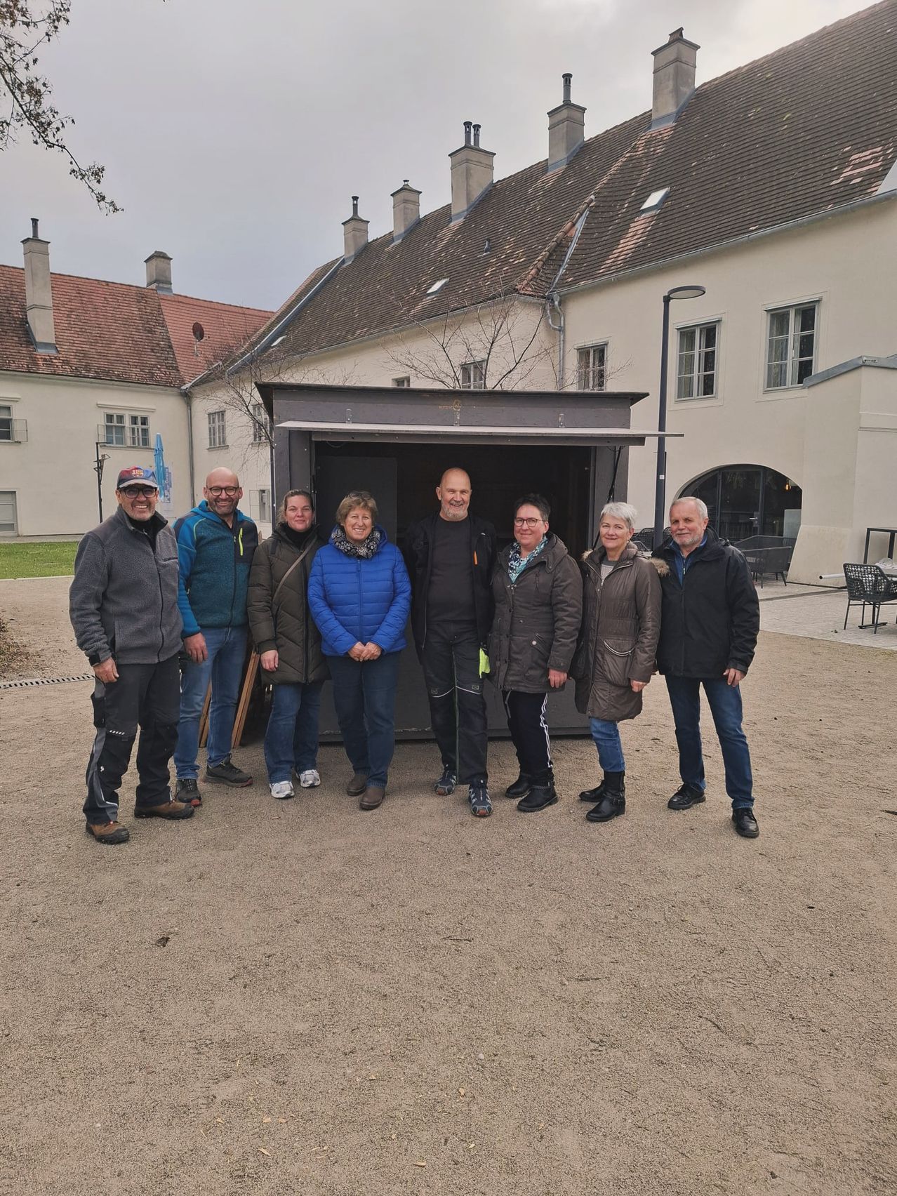 Eine Gruppe von Menschen steht vor einem Gebäude, in Wintermänteln und Stiefeln gekleidet. Sie scheinen für ein Foto zu posieren.