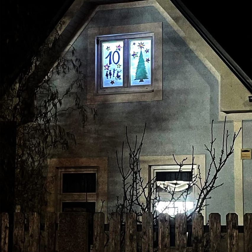 Ein Haus mit einem Fensterdisplay, das die Nummer 10 und einen Weihnachtsbaum mit Sternen zeigt, beleuchtet in der Nacht.