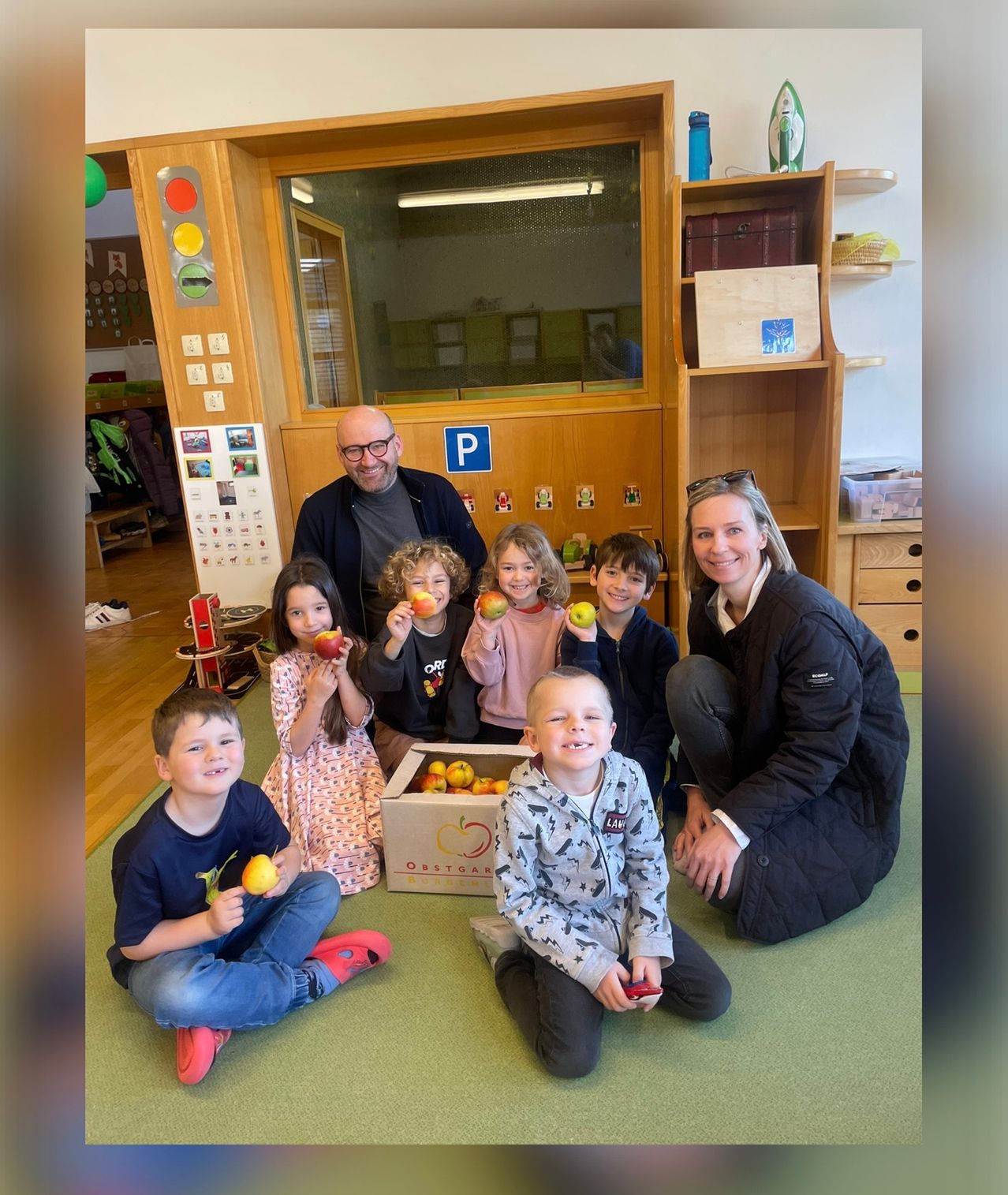 Eine Gruppe von Kindern und zwei Erwachsenen posiert mit Äpfeln in einem Klassenzimmer für ein Foto.