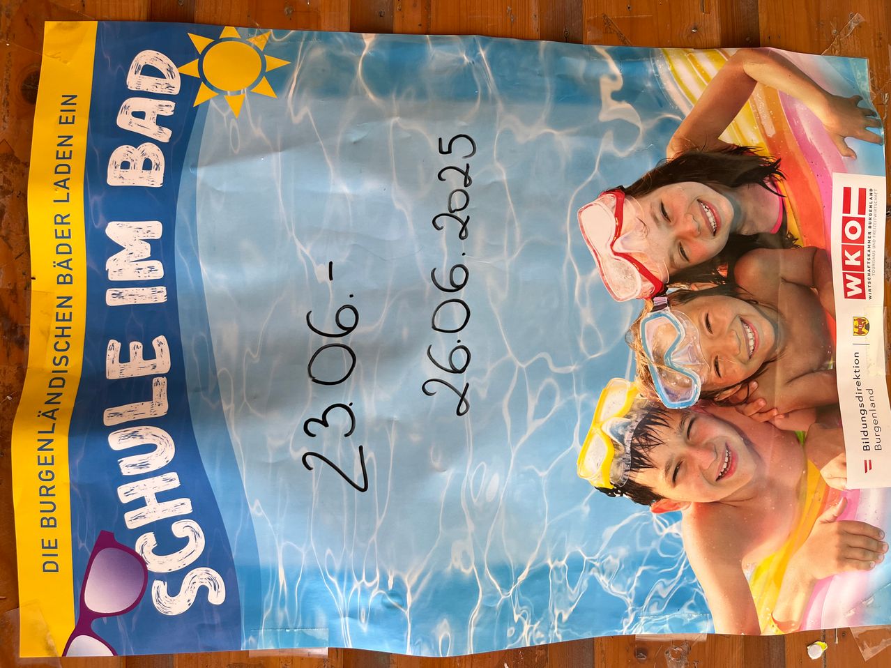 Ein Poster mit Pool-Thema zeigt drei lächelnde Kinder mit Schwimmbrillen. Die Daten 23.06 und 26.06.2025 sind angezeigt, und das Wort 'SCHWIMMBAD' ist prominent dargestellt.
