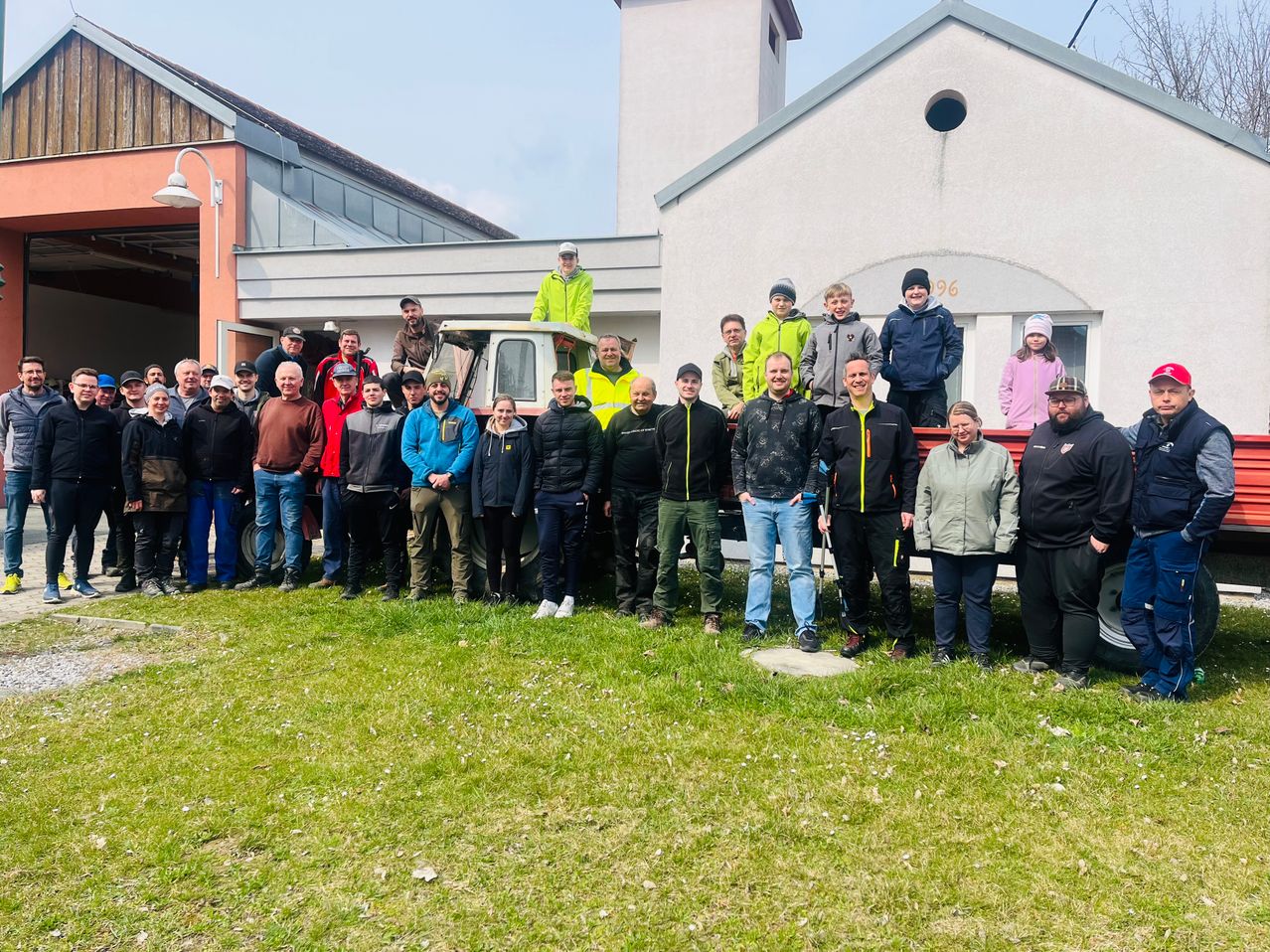 Eine Gruppe von Menschen in Winterkleidung posiert für ein Foto vor einem Gebäude mit einem Traktor.