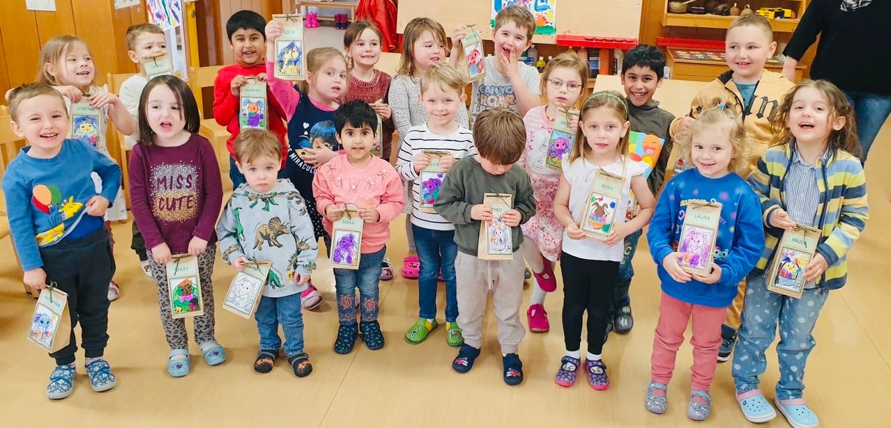 Eine Gruppe von Kindern in einem Klassenzimmer, die Zeichnungen mit ihren Namen halten, einige lächeln und andere posieren für ein Foto.