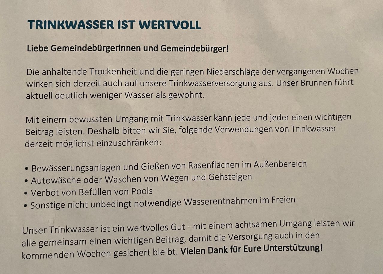 Ein Flyer mit blauem Text lautet 'TRINKWASSER IST WERTVOLL' in Fettdruck. Es enthält eine Liste vorgeschlagener Wassersparmaßnahmen. Der darunterstehende Text ist in kleinerer Schrift und erklärt die derzeitige Trinkwasserknappheit. Der Flyer endet mit einem Dank für die Unterstützung.