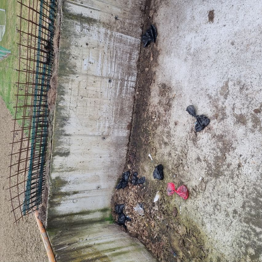 Ein Blick von oben auf eine Betonwand mit einem Metallzaun. Mehrere Plastiktüten, einschließlich einer roten, sind auf dem Boden verstreut.