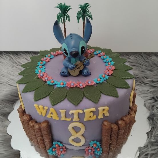 Ein Geburtstagskuchen für Walter mit einer blauen Stitch-Figur, die eine Gitarre spielt, umgeben von bunten Blumen und Palmen. Der Kuchen hat eine lila Basis und braune Akzente.