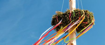 Eine bunte Bandschleife hängt an einem Pfosten am blauen Himmel, möglicherweise für ein Festival.