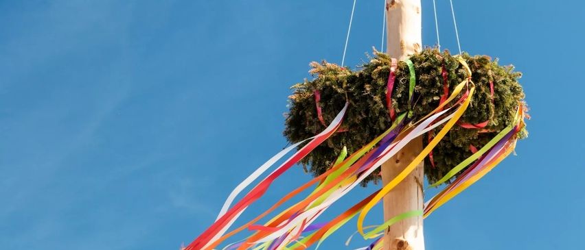 Eine bunte Bandschleife hängt an einem Pfosten am blauen Himmel, möglicherweise für ein Festival.