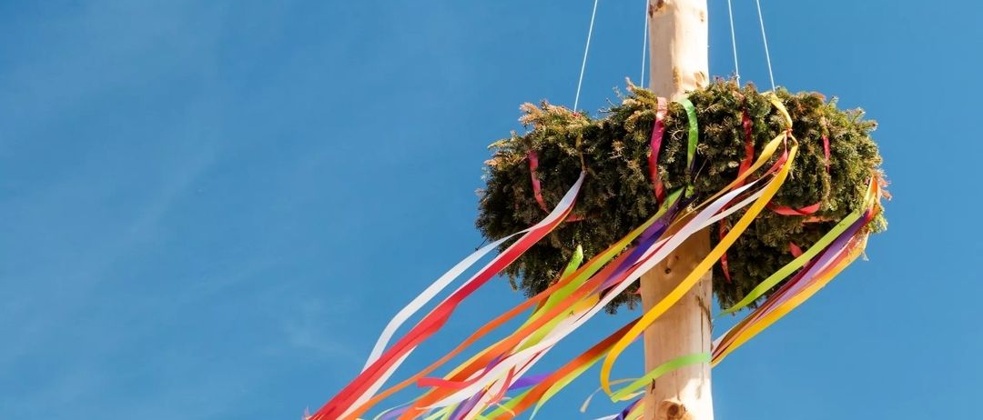 Eine bunte Bandschleife hängt an einem Pfosten am blauen Himmel, möglicherweise für ein Festival.