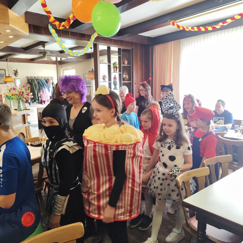 Eine Gruppe von Kindern in Kostümen steht in einem Restaurant. Ein Kind ist als Popcorn-Eimer verkleidet.