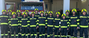 Eine Gruppe Feuerwehrleute in Uniform posiert für ein Foto vor einem Feuerwehrwagen. Der Wagen trägt den Namen St. Georg/STFG.