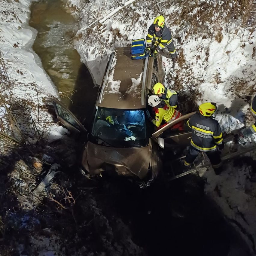 Ein Auto ist in einem Bach stecken geblieben, während Rettungskräfte den Fahrer bei verschneiten Bedingungen retten.