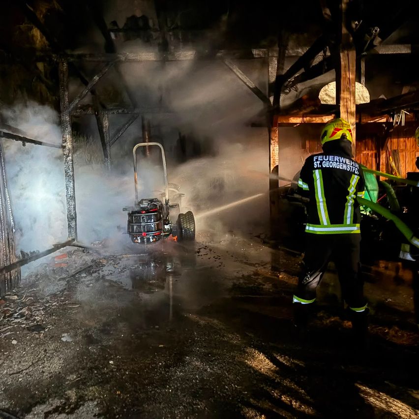 Ein Feuerwehrmann aus St. Georgen löscht einen Brand in einer Scheune mit einem Schlauch. Rauch füllt die Luft, und ein Feuerlöscher ist in der Nähe.