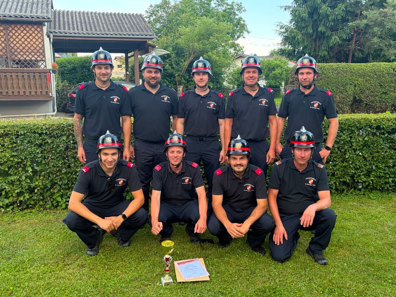 A group of firefighters in uniform posing for a photo with a trophy and certificate in front of them.