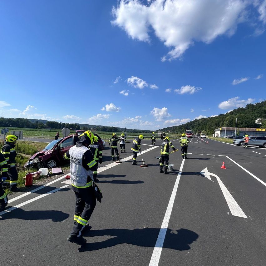 Rettungskräfte räumen die Unfallstelle eines Autounfalls auf der Straße unter blauem Himmel mit verstreuten Wolken auf.