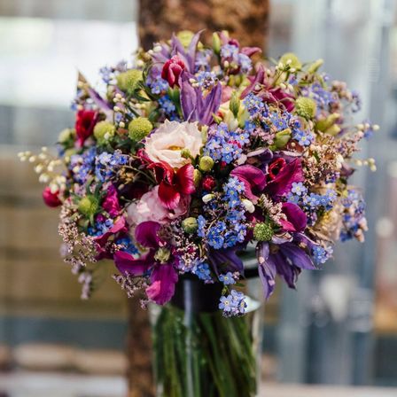Ein farbenfroher Strauß aus verschiedenen Blumen, darunter lila, rosa und blaue Blüten, präsentiert in einem klaren Glasvase.