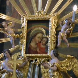 Ein goldener Rahmen mit einem Gemälde der Jungfrau Maria und Jesu, umgeben von Cherubs und Kerzen.