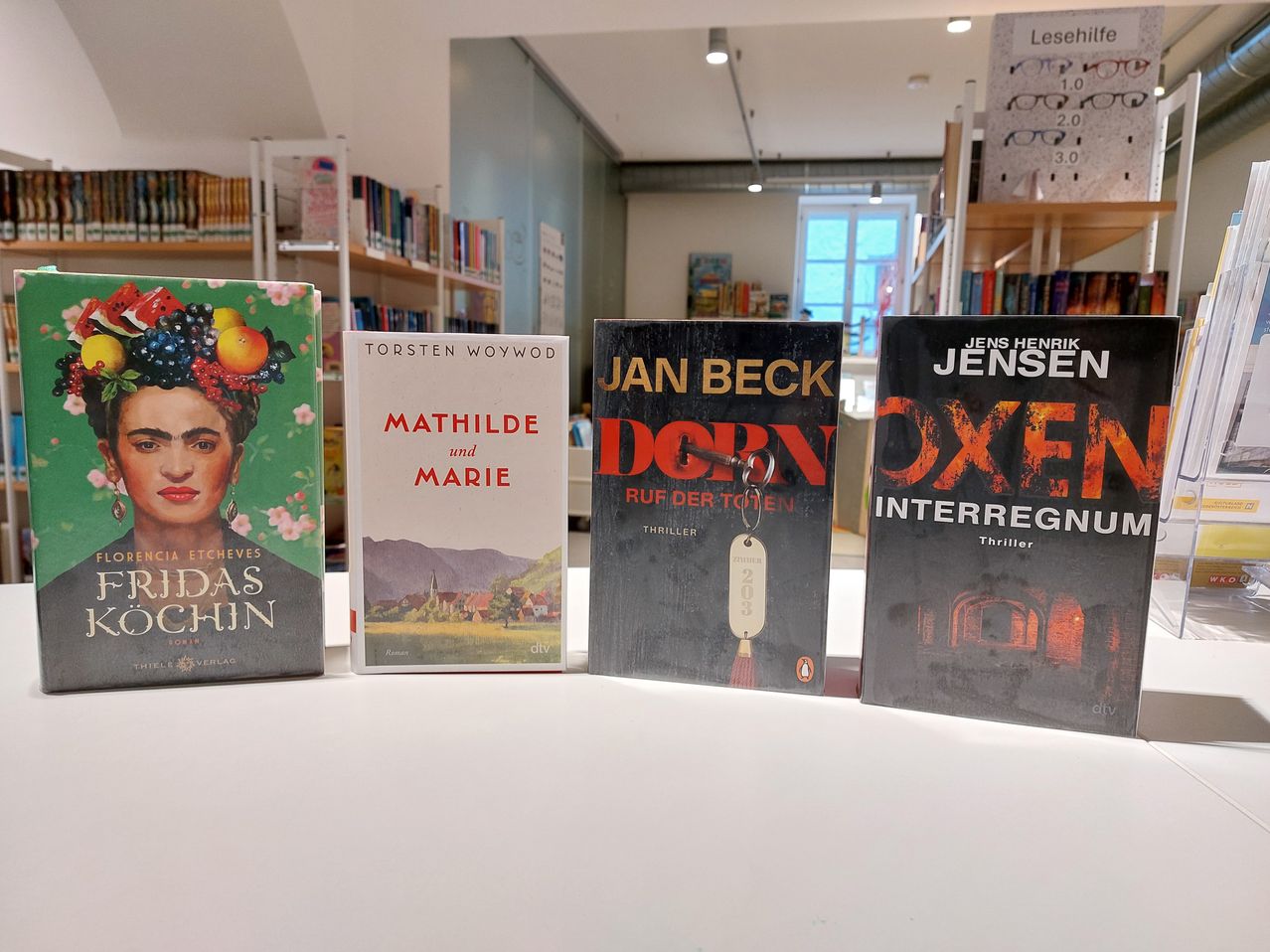 Four books are displayed on a white table in a bookstore. The books are titled 'Idaas Chin', 'Matilde und Marie', 'Jan Beck Dorn', and 'Jens Henrik Jensen Oxen Interregnum'.
