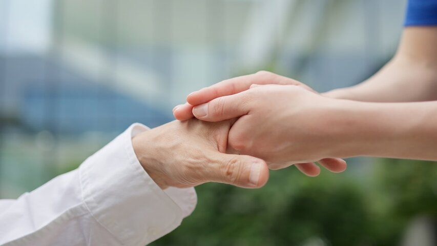 Eine Hand wird von einer anderen Person, wahrscheinlich einem Arzt, in einem Büro gehalten.