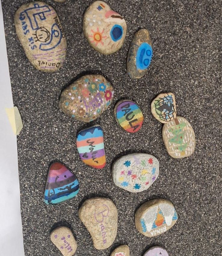 Verschiedene Steine mit Zeichnungen und Aufschriften liegen auf einer grauen Oberfläche. Sie haben verschiedene Muster, Worte und Symbole.
