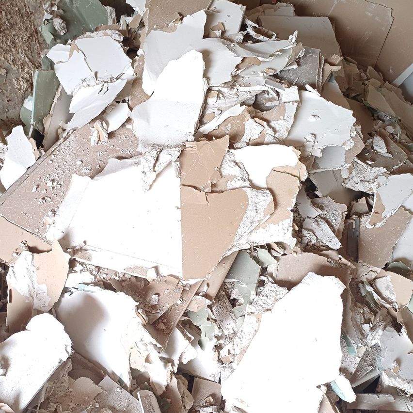 Ein Haufen zerbrochener Gipskartonplatten, von denen einige weiß und andere braun sind, verstreut auf dem Boden.