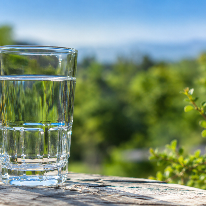 Ein klares Glas Wasser auf einer Holzoberfläche mit einem verschwommenen grünen Hintergrund.