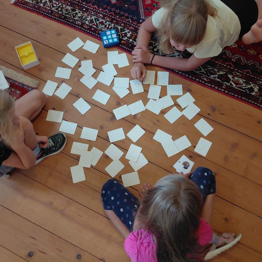 Three young girls are playing a card game on a wooden floor. The cards are scattered around them, and they are engaged in the game.