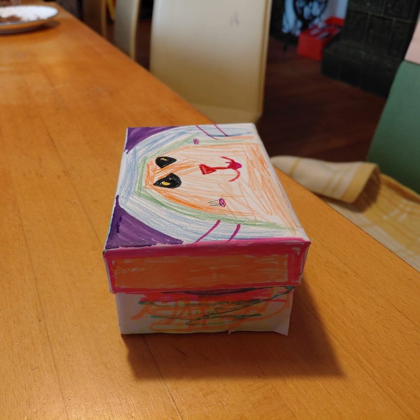 A small box with a colorful drawing of a face on it, placed on a wooden table.