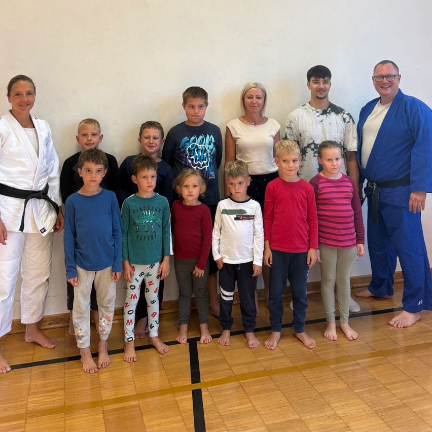 A group of young boys and girls in martial arts uniforms pose for a photo with their instructors in a gym.