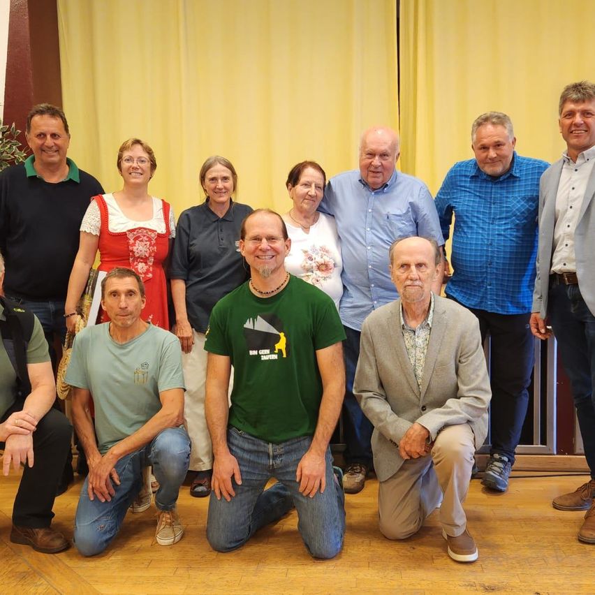 Eine Gruppe von Menschen posiert für ein Foto. Sie lächeln und stehen vor einem gelben Vorhang.