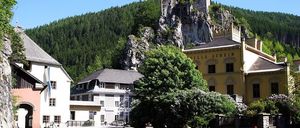 Eine kleine Stadt mit einer Burg auf einem felsigen Felsvorsprung darüber, umgeben von Bäumen. Ein gelbes Gebäude mit 'VILLA AUHEI' darauf.