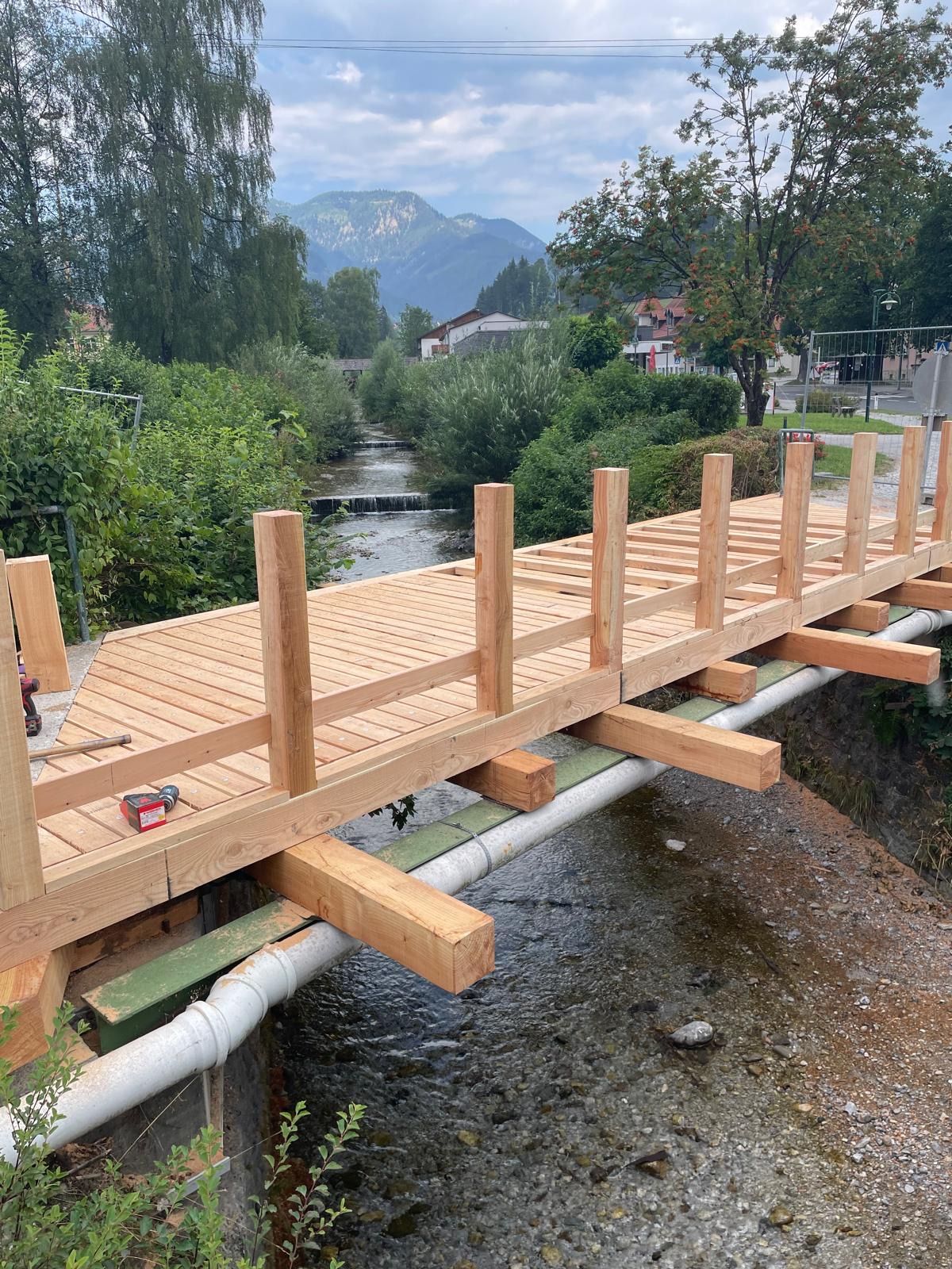A wooden bridge under construction over a small river with mountains in the background.