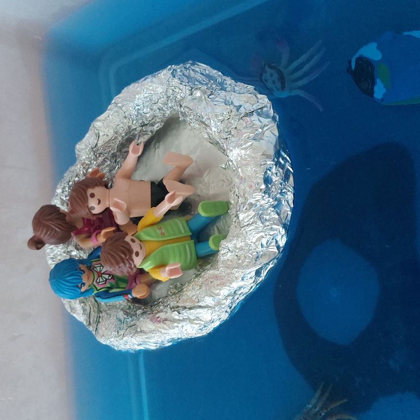 Vier Playmobil-Figuren liegen in einem silbernen Foliennest auf blauem Hintergrund.