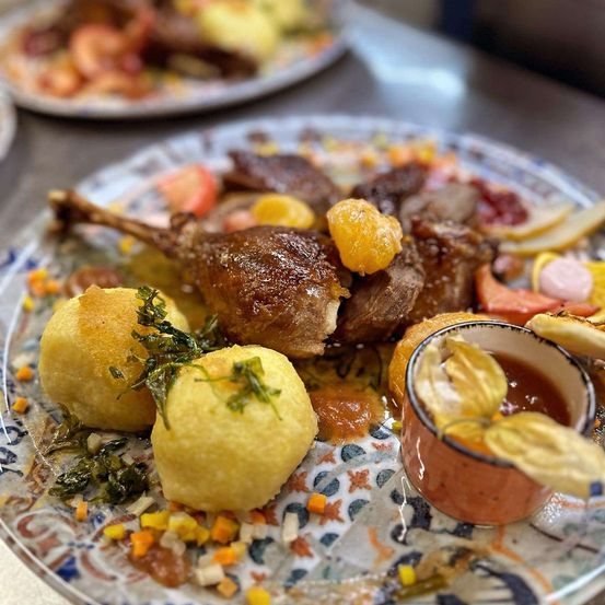 Ein servierter Teller mit Entenfleisch, Kartoffeln und Orangenscheiben. Ein kleiner Saucenbecher und Garnierungen sind ebenfalls auf dem Teller.