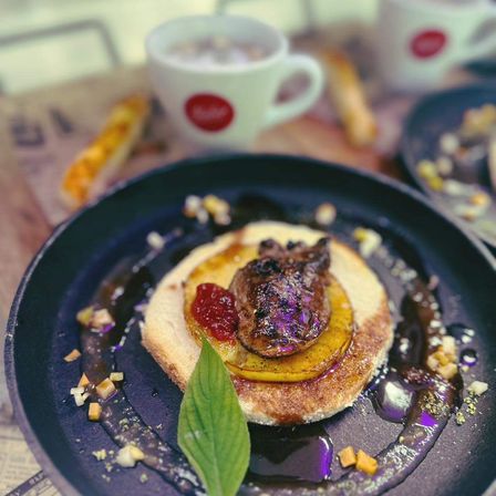 Ein Gericht mit Fleisch auf einem runden Teller, mit Brot, Marmelade und Sauce, begleitet von einer Tasse Kaffee.