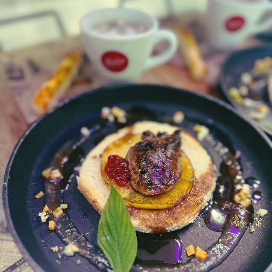Ein Gericht mit Fleisch auf einem runden Teller, mit Brot, Marmelade und Sauce, begleitet von einer Tasse Kaffee.