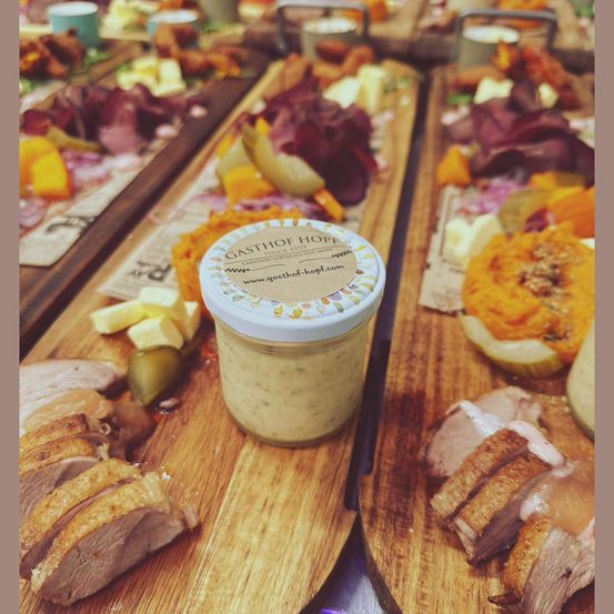 Auf einem Holztisch sind verschiedene Fleischsorten, Käse, Gemüse und ein mit Gasthof Hopp beschriftetes Glas zu sehen.
