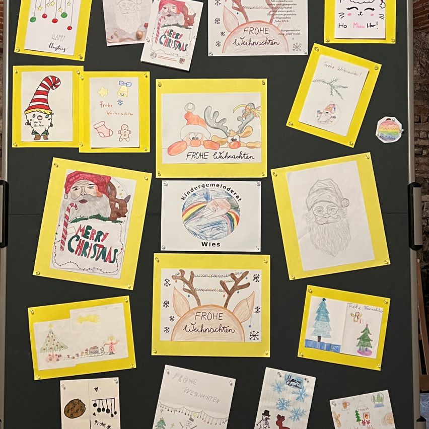 Ein Bulletinbrett zeigt verschiedene handgezeichnete Weihnachtskarten mit festlichen Dekorationen, einschließlich Weihnachtsmann, Rentiere, Schneeflocken und Weihnachtsbäumen, in einem Raster angeordnet. Jede Karte hat einzigartige Kunstwerke und Texte wie Merry Christmas, Frohe Weihnachten und Kindergemeindeat Wies.