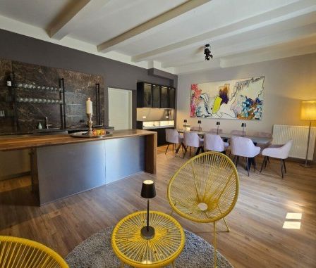 Modernes Interieur mit Holzboden, bestehend aus einer Kücheninsel, einem Essbereich mit Stühlen und einem großen abstrakten Gemälde an der Wand.