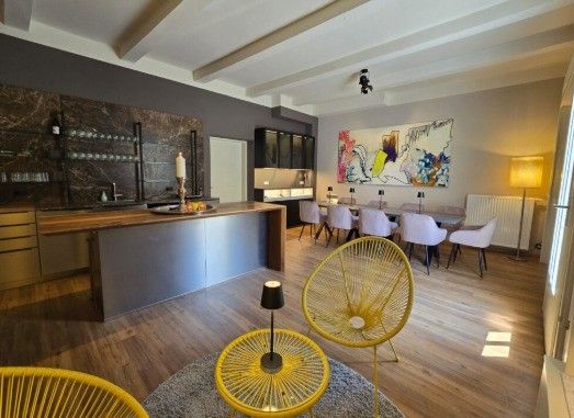 Modernes Interieur mit Holzboden, bestehend aus einer Kücheninsel, einem Essbereich mit Stühlen und einem großen abstrakten Gemälde an der Wand.