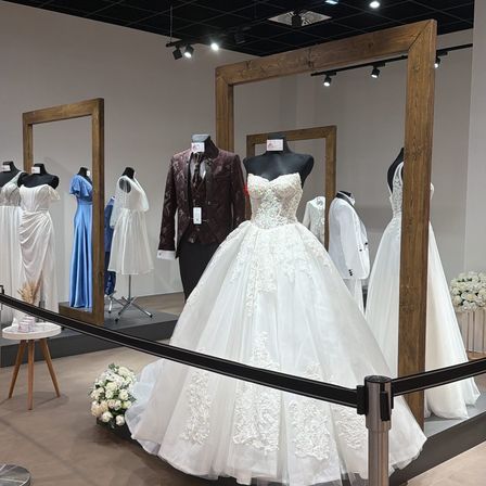 Ein Hochzeitskleid an einem Mannequin wird in einem Geschäft ausgestellt. Mehrere Brautkleider und Anzüge sind auf den Mannequins hinter der Scheibe ausgestellt.