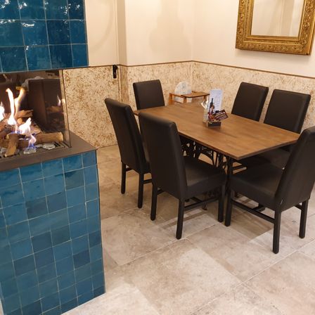 Ein Essbereich mit einem Holztisch und schwarzen Stühlen, einem Kamin links und einem Spiegel an der Wand.