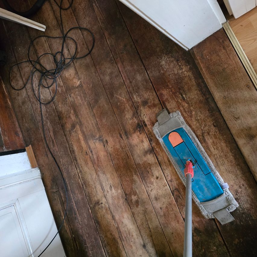 Ein Mopp wird zum Reinigen eines Holzbodens verwendet. Der Boden hat einige Flecken und Schmutz.